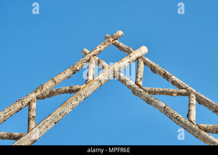 Wooden fence and gate made of old dry thin logs against a blue sky. Rural scene Stock Photo