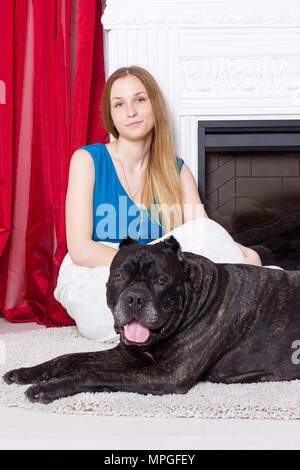 Girl in blue dress sitting by the fireplace with a dog Cane Corso Stock Photo