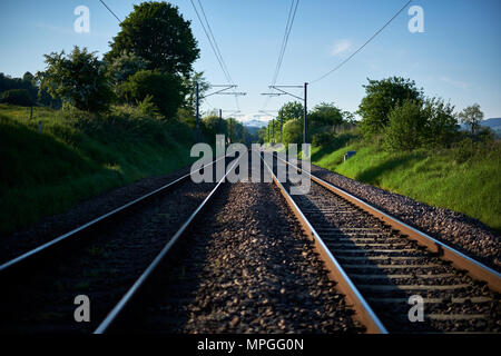 Looking down a pair of train tracks through countryside on a clear evening Stock Photo