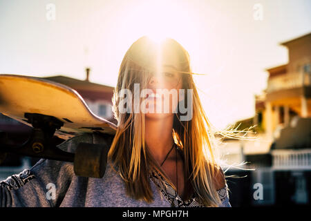 nice portrait for a beautiful long blonde hair young woman with her skateboard on the shoulder. rebel and sunny day of vacation concept. travel and en Stock Photo