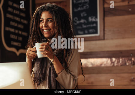 Smiling woman standing in a cafe holding a cup of coffee. Stock Photo