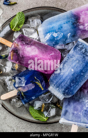 Naturally organic summer sweets, homemade blue and violet ice cream popsicles with butterfly pea flower tea, grey concrete background copy space Stock Photo