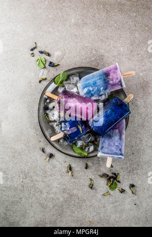 Naturally organic summer sweets, homemade blue and violet ice cream popsicles with butterfly pea flower tea, grey concrete background copy space Stock Photo