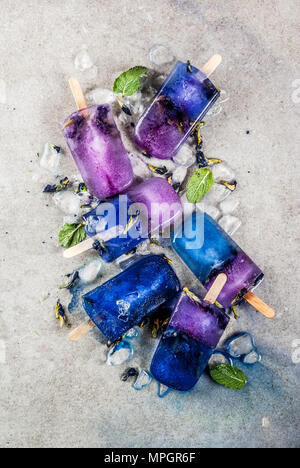 Naturally organic summer sweets, homemade blue and violet ice cream popsicles with butterfly pea flower tea, grey concrete background copy space Stock Photo