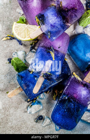 Naturally organic summer sweets, homemade blue and violet ice cream popsicles with butterfly pea flower tea, grey concrete background copy space Stock Photo