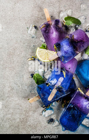 Naturally organic summer sweets, homemade blue and violet ice cream popsicles with butterfly pea flower tea, grey concrete background copy space Stock Photo