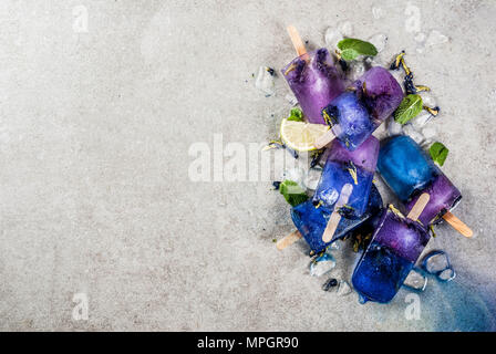 Naturally organic summer sweets, homemade blue and violet ice cream popsicles with butterfly pea flower tea, grey concrete background copy space Stock Photo