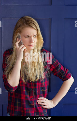 Pretty Woman Calling Someone Through Mobile Phone While Smiling at the Camera Against Blue Wall Background Stock Photo