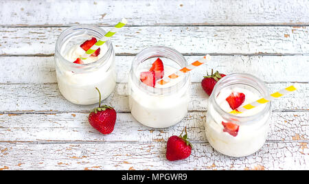 Three jars of yogurt with strawberries and colored tubes on a wooden board Stock Photo