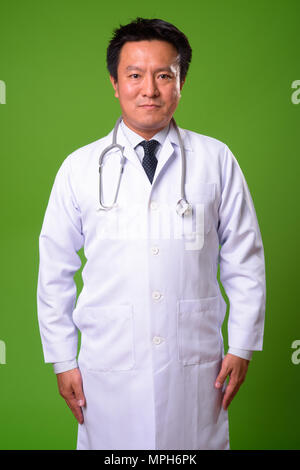 Mature Japanese man doctor against green background Stock Photo