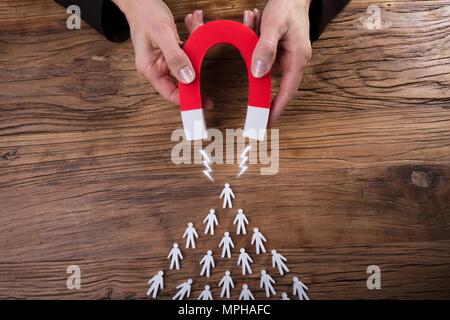 Businessperson's Hand Attracting Human Figures With Horseshoe Magnet On Wooden Desk Stock Photo