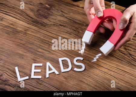 Businessperson Attracting White Lead Text With Horseshoe Magnet Over Wooden Desk Stock Photo