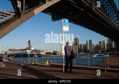 07.05.2018, Sydney, New South Wales, Australia - A man waits at a bus stop at Milsons Point and looks at the Sydney Harbour Bridge and the skyline. Stock Photo