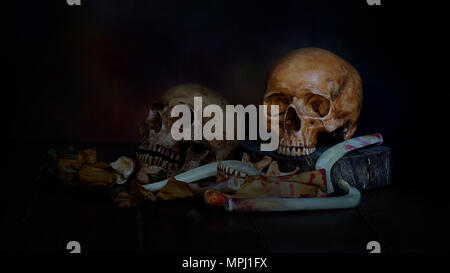 pile of two human skull and skeleton wit dry rose flower on old wood background,concept in died because of love Stock Photo