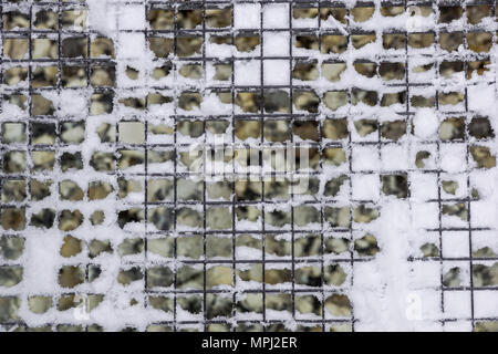 drain grate for water drainage in city streets, metal grid, iron manhole, covered with snow during a storm, blizzard, winter, mountain Stock Photo