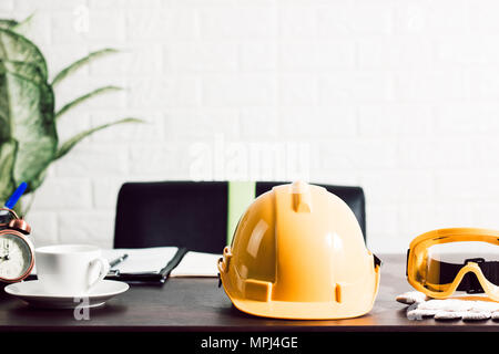 helmet and glass of engineer on table in office with copy space of white brick wall background Stock Photo