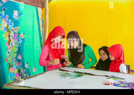 Krabi, Thailand - May 2, 2015: Beautiful Muslim woman wearing red hijab painting pattern on Batik fabric in her home in Krabi, Thailand Stock Photo