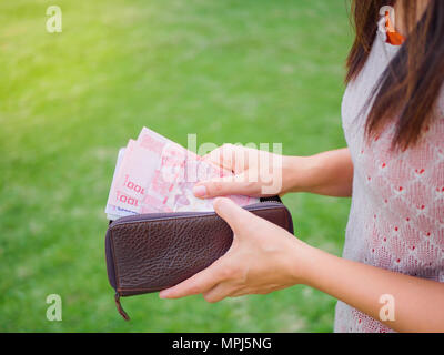 Women Hands taking out money thai baht from wallet on the green grass field Stock Photo