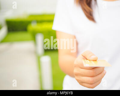 Closeup of woman's hand inserting e-card into ATM slot on the green grass background Stock Photo