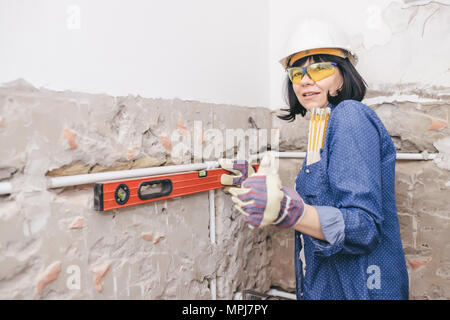 Smiling woman repairing her bathroom sink pipe with  positive attitude. Woman using  Bubble Spirit Water Ruler Tool while setting up and checking the  Stock Photo
