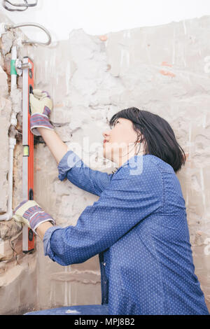 Clever woman repairing her bathroom sink pipe with  positive attitude. Woman using  Bubble Spirit Water Ruler while setting up and checking the tubes  Stock Photo