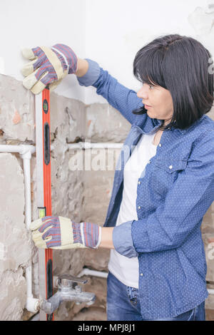 Clever woman repairing her bathroom sink pipe with  positive attitude. Woman using  Bubble Spirit Water Level Construction Tool while setting up and c Stock Photo