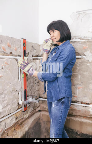 Clever woman repairing her bathroom sink pipe with  positive attitude. Woman using  Bubble Spirit Water Level Construction Tool while setting up and c Stock Photo
