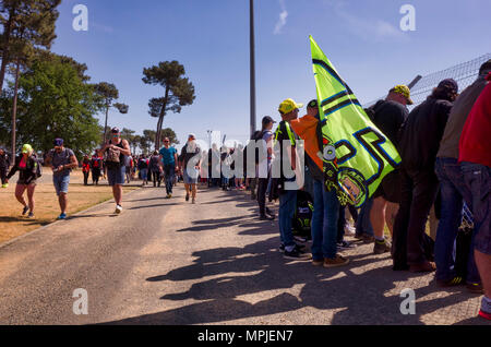 19-20th May 2018. Le Mans, France.  Behind the scenes at the MotoGP.  Spectators line the perimeter fence of the race circuit to watch the MotoGP practice session.  Meanwhile, other fans walk along the dirt road behind in search of refreshments or alternative viewing locations.  One of the spectating fans holds a number 46 flag, demonstrating his support of Valentino Rossi. Stock Photo