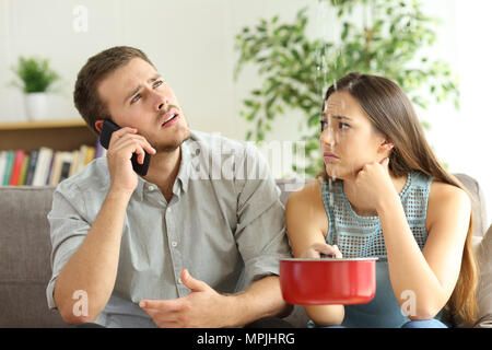 Desperate couple callling to insurance worried about home leaks in the living room Stock Photo