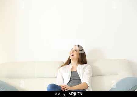 Wide angle view portrait of a woman sitting on couch and looking above with copy space Stock Photo