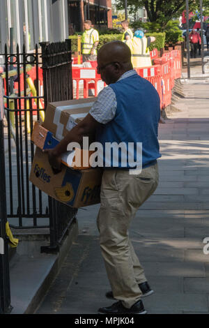 A man of Afro-Caribbean ethnicity carrying a pile of boxed and delivering packages to address in central London. Heavy lifting delivery man on rounds. Stock Photo