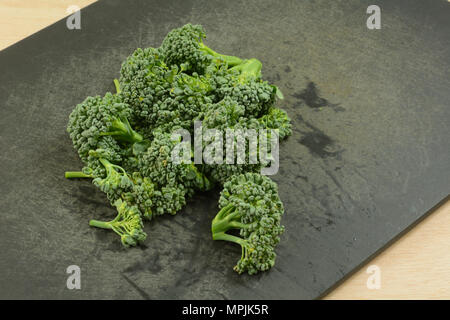 Chopped freshly rinsed raw broccoli florets on black weathered cutting board Stock Photo