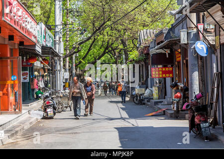 A pair of workmen stroll down a street in Beijing. One exposes his abdomen in order to cool down in the midday heat. Stock Photo