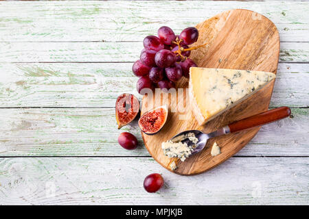 Stilton on a cheese board with red grapes and cheese spoon, top view Stock Photo