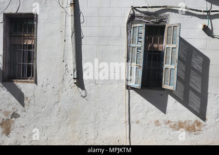 Ancient white house with vintage windows, metal grilles and wooden shutters on the windows, from which an oblique shadow falls on the wall. Stock Photo