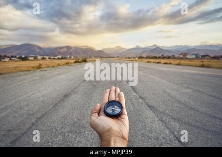 Traveler holding compass on the road with mountains at sunrise sky background. Travel and adventure concept. Stock Photo
