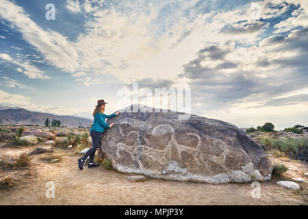 Tourist girl in checkered shirt in the open air museum near stone with ancient petroglyph of goats at Kyrgyzstan Stock Photo