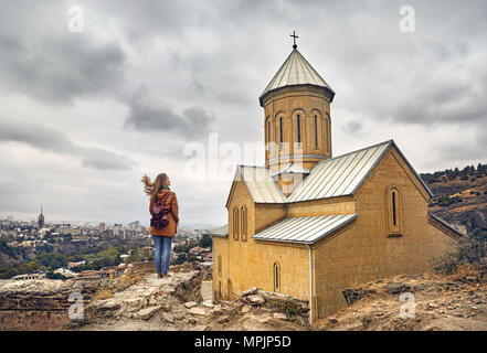 Tourist woman near Cathedral in Old medieval castle Narikala at overcast cloudy sky in Tbilisi, Georgia Stock Photo