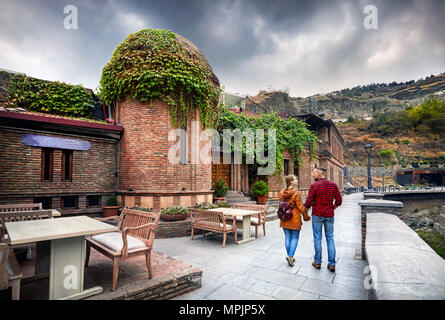 Tourist woman in brown jacket and man in red shirt walking down the Old streets of Public Sulfuric bath district in central Tbilisi, Georgia Stock Photo