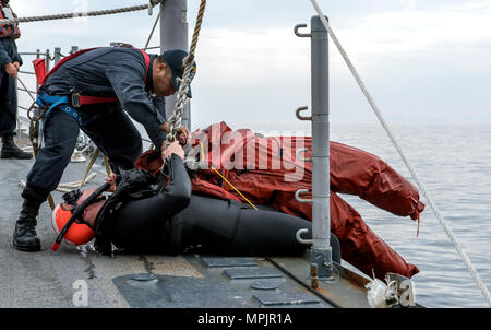 170318-N-FT187-060 KOREA STRAIT (March 18, 2017) Boatswain's Mate 2nd Class Marte Pena, from Bronx, New York, pulls Sonar Technician (Surface) 2nd Class Paden Meinhold, a search and rescue swimmer, from Loveland, Colorado, and a simulated victim onto the forecastle of Ticonderoga-class guided-missile cruiser USS Lake Champlain (CG 57) during a man overboard training evolution. Lake Champlain is on a regularly scheduled Western Pacific deployment with the Carl Vinson Carrier Strike Group as part of the U.S. Pacific Fleet-led initiative to extend the command and control functions of the U.S. 3rd Stock Photo