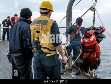 170318-N-FT187-057 KOREA STRAIT (March 18, 2017) Boatswain's Mate 2nd Class Marte Pena, from Bronx, New York, grabs the line as Sonar Technician (Surface) 2nd Class Paden Meinhold, a search and rescue swimmer, from Loveland, Colorado, brings a simulated victim up to the forecastle of Ticonderoga-class guided-missile cruiser USS Lake Champlain (CG 57) during a man overboard training evolution. Lake Champlain is on a regularly scheduled Western Pacific deployment with the Carl Vinson Carrier Strike Group as part of the U.S. Pacific Fleet-led initiative to extend the command and control functions Stock Photo