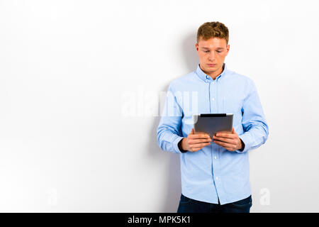 Young man using tablet and standing against white wall. Stock Photo