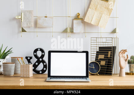 Mockup of laptop on wooden desk with clock, plants and pots in workspace interior Stock Photo