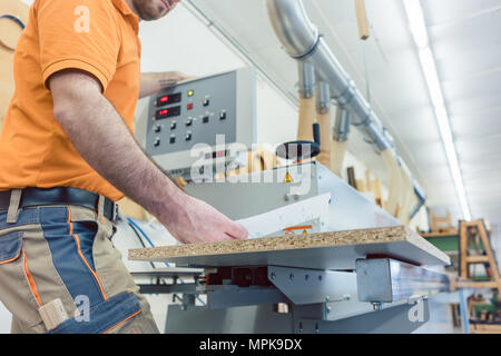 Carpenter in furniture factory pressing button on machine Stock Photo