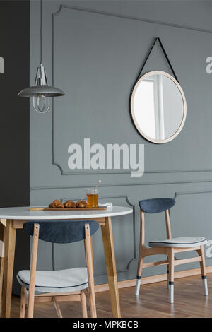 Wooden chairs against grey wall with molding and round mirror in simple dining room interior Stock Photo