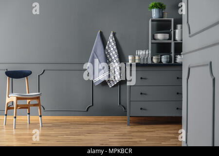 Wooden chair against grey wall with molding and textiles in kitchen interior with cabinet Stock Photo