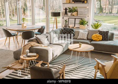 High angle view of a stylish, nordic living room interior with a wooden dining table, gray sofa and view on terrace and backyard. Real photo Stock Photo