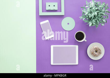 Plant, doughnut and cup of coffee on violet desk with mockup of tablet and smartphone Stock Photo