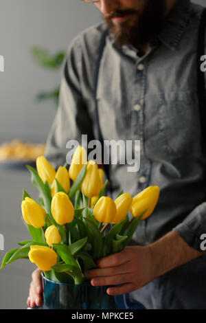 Close-up of man in grey shirt putting yellow tulips into vase Stock Photo