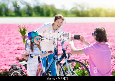 Dutch family riding bicycle in tulip flower fields in Netherlands. Mother and kids taking selfie picture with mobile phone camera on bikes at blooming Stock Photo